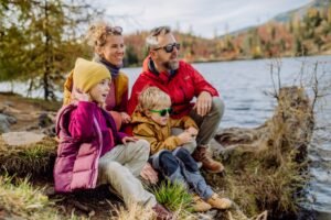 Happy young family with little children, resting near lake in mountains.