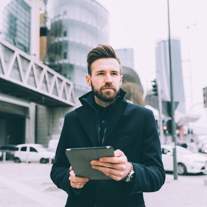 Young successful bearded business man outdoor using tablet